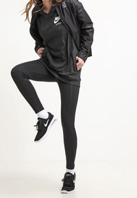 Black athletic wear featuring a hooded top and fitted leggings, paired with black sneakers. The jacket has a textured design.