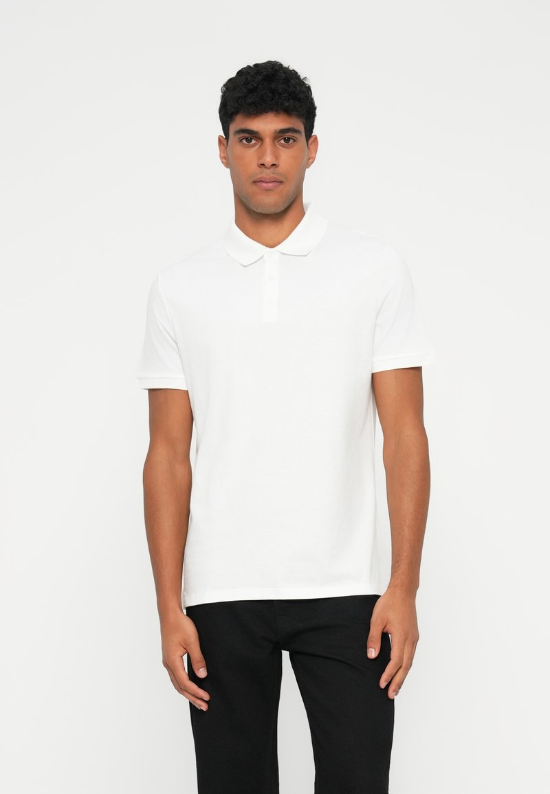 Camisa polo branca feita de algodão, com colarinho clássico, com três botões, mangas curtas e barra reta.