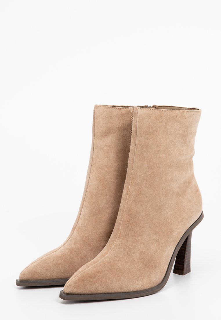Botines de ante beige con punta afilada y tacón apilado. Presentan una textura suave y cierre de cremallera en la parte posterior.