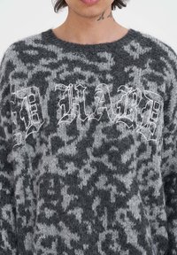 Grijze en zwarte gebreide trui met een pluizige textuur, luipaardprint en gedurfde witte letters met de tekst "ID HARD." Ronde halslijn.