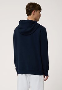 Sudadera azul marino hecha de un tejido suave, con una capucha espaciosa, puños acanalados y un corte relajado, mostrada desde la parte de atrás.
