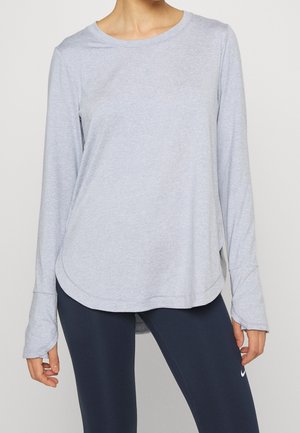 Person iført lysegrå langærmet trøje med hul til tommelfingre og mørkeblå leggings med hvidt Nike-logo.