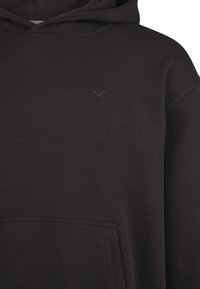 Black hoodie made of ribbed fabric, featuring a kangaroo pocket and a small embroidered logo on the chest. Simple, relaxed fit design.