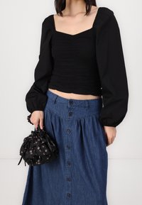 Haut noir froncé avec un décolleté carré, associé à une jupe en denim avec des boutons. Tient un sac à cordon fleuri noir.