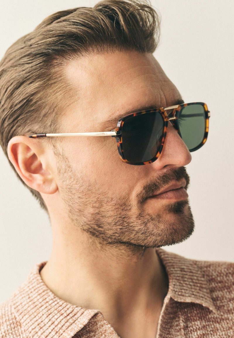 Tortoiseshell sunglasses with dark lenses. Thin metallic arms in silver accent. Square shape with rounded edges, showcasing a modern design.