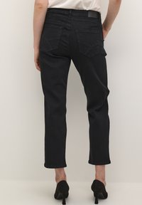 Jean en denim noir avec une coupe droite, taille mi-haute, deux poches arrière et des détails de couture subtils. Associé à des chaussures à talons hauts noires.