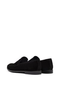 Mocassins en suède noir avec une semelle en caoutchouc plate, présentant un design à enfiler et un minimum de coutures. Texture lisse avec une silhouette classique.