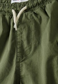 Shorts verdi in cotone con vita elastica, cordino crema e tasca laterale, caratterizzati da una consistenza liscia e semplici dettagli di cucitura.