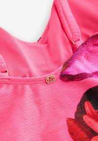 Jasnoróżowy strój z teksturowaną powierzchnią, zdobiony wzorem kwiatowym i małym złotym zapięciem na pasku.