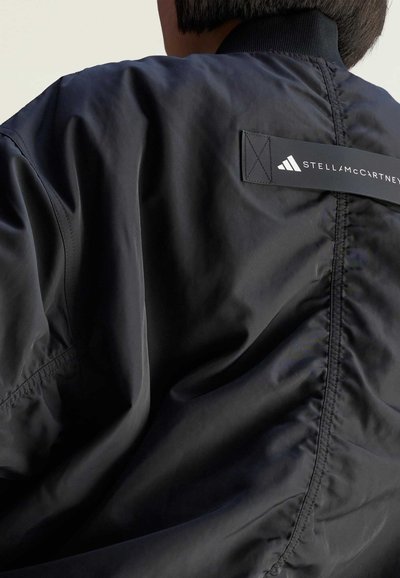 Černá bomber jacket s elegantní tkaninou hladké struktury, vyšívaným logem a značkováním výrazně viditelným na zadní straně.