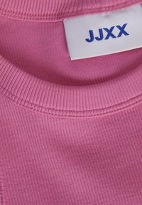 Rausvos spalvos briaunotas švarkas su apvalia iškirpte ir mėlynu ženkleliu „JJXX“. Audinys yra minkštas ir lanksčius.