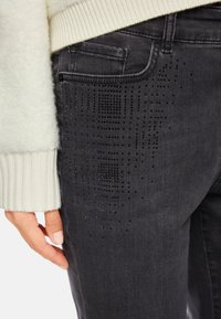 Schwarze Jeans aus Denim mit einem strukturierten Muster aus kleinen Nieten an der Seite, begleitet von einem leichten Strickpullover mit gerippten Bündchen.