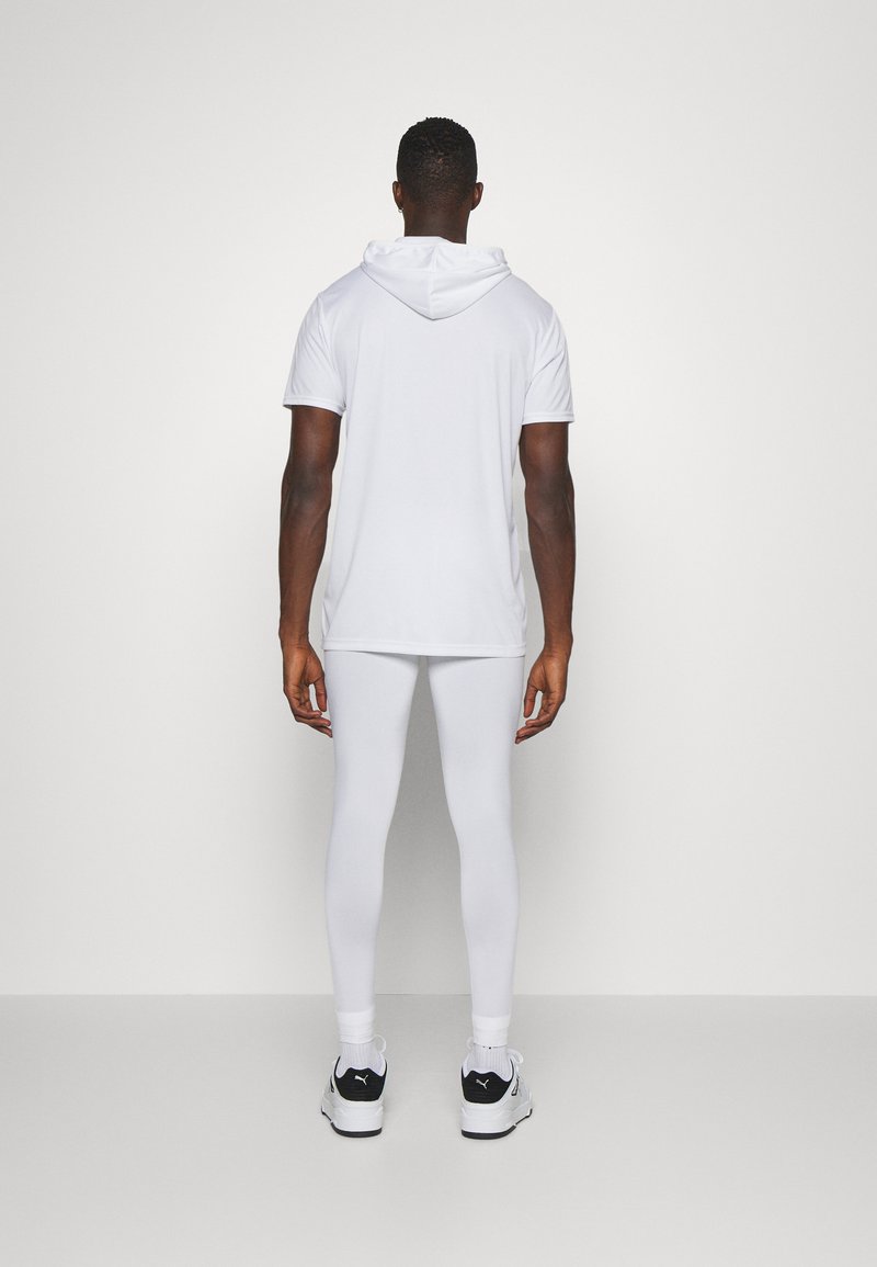 Felpa bianca a maniche corte con cappuccio, abbinata a leggings bianchi, indossata con scarpe da ginnastica nere e bianche, vista da dietro.