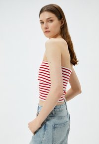 Top bandeau a rayas rojas y blancas con un diseño plegado, combinado con pantalones vaqueros de mezclilla clara de cintura alta. Textura suave, ajuste casual.