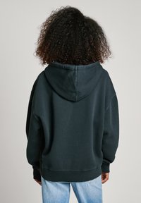 Hoodie noir surdimensionné en mélange de coton doux, avec une capuche à cordon, des poignets côtelés et une coupe décontractée, associé à un jean bleu clair.