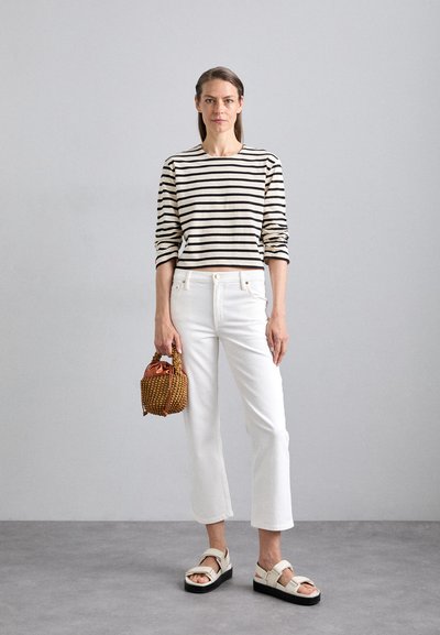 Striped, cropped boatneck sweater in cream and black, paired with white straight-leg jeans. Brown woven handbag and chunky sandals complete the look.