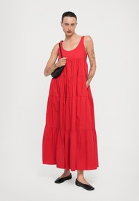 Abito maxi rosso a strati con spalline larghe e vestibilità ampia. Realizzato in cotone, presenta un design arricciato e due tasche laterali. Abbinato a ballerine nere.