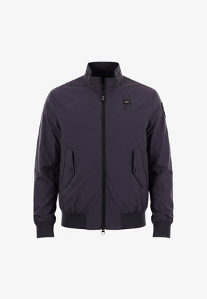 Veste bomber bleu marine foncé avec fermeture éclair à l'avant, deux poches à rabat avec boutons, poignets et ourlet côtelés, et un petit écusson sur la poitrine et la manche.
