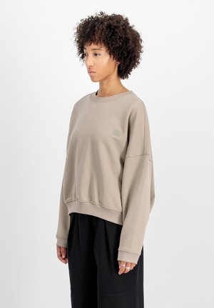 Felpa beige con vestibilità casual, polsini e orlo a costine, con una piccola toppa del logo sul petto. Tessuto morbido e texturizzato.