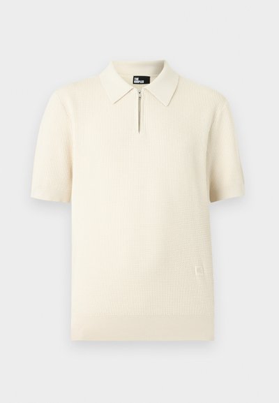 Polo en maille couleur crème à manches courtes, motif texturé, patte zippée, col, poignets et bas-côte.