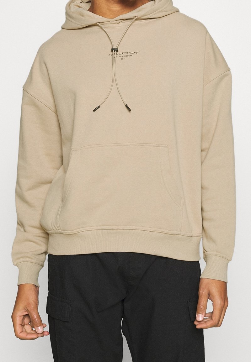 Sudadera con capucha de algodón beige con bolsillo tipo canguro, capucha con cordón y logo impreso. Cuenta con puños y dobladillo acanalados, textura suave.