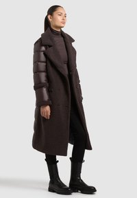 Tumepruun, pikk mantel tekstuurse, udusa välispinnaga ja läikivate puffer-varrukatega. Omadusteks suur krae ja topelt nööbimiskohad.