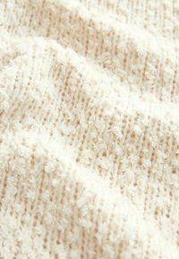 Tissu crème texturé avec un motif tricoté comportant des zones en relief et duveteuses. Doux et moelleux avec une apparence chaleureuse et accueillante.