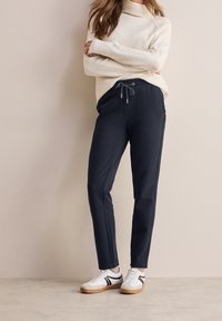 Navy trousers with elasticated waistband and drawstring, featuring side pockets. Paired with a cream turtleneck sweater and sneakers.