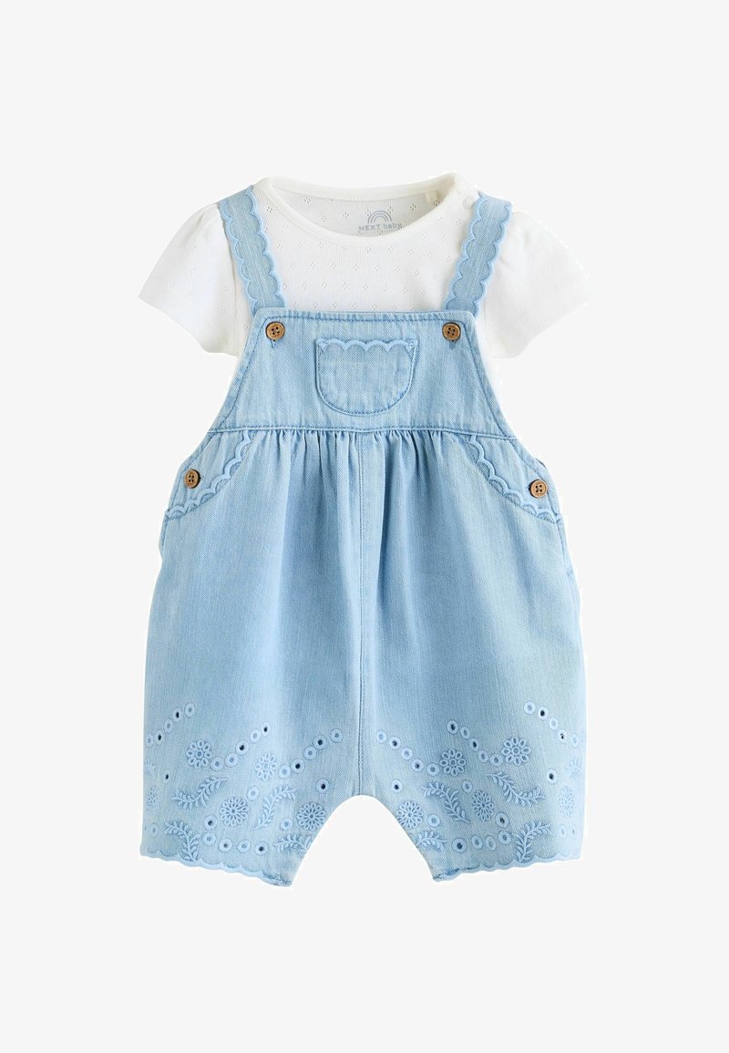 Biała koszulka niemowlęca z krótkim rękawem w połączeniu z jasno niebieskimi, haftowanymi ogrodniczkami dżinsowymi z falowanymi krawędziami i drewnianymi guzikami.