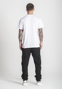 Biely bavlnený tričko s krátkym rukávom, spárované s čiernymi cargo nohavicami so vreckami. Model má na sebe biele tenisky s Modrými akcentmi.