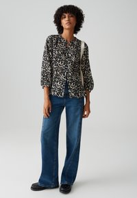 Camicia a maniche tre quarti a righe bianco e nere, abbinata a jeans blu a vita alta e scarpe nere.