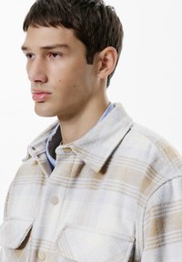 Flannel shirt in light gray with yellow and white plaid pattern, featuring a button-up collar and two front pockets. Soft texture.