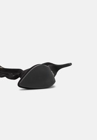 Zapato de tacón alto negro con parte superior de ante, punta afilada y suela de goma triangular. El tacón es delgado y elevado, mostrando un diseño elegante.