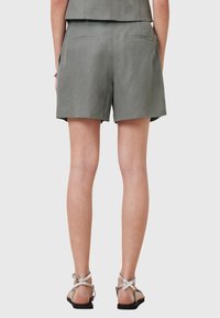 Shorts en lin gris avec une coupe ample, poches latérales et poches arrière décoratives. Portés avec des sandales plates en strass argentées.