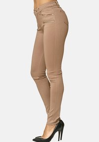 Bruna skinny jeans i stretchy material med zippered pockets och subtil sömdetaljering. Kombineras med svarta högklackade skor.