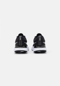 Zapatillas deportivas en blanco y negro con parte superior de malla, suela acolchada, diseño aerodinámico y acentos reflectantes en la parte trasera.