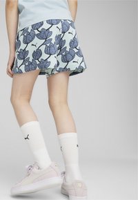 Shorts florales azules y verdes de corte suelto, combinados con calcetines blancos y zapatillas rosa claro. Presenta un logo visible cerca del dobladillo.