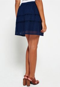 Granatowa spódnica koronkowa z warstwowym wzorem i teksturowanym printem, z elastycznym pasem, w połączeniu z brązowymi sandałami na obcasie.