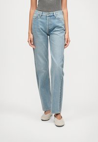 Jean droit bleu clair en denim, avec des détails de couture latérale comportant de petits découpes circulaires. Design taille haute avec poches standard.