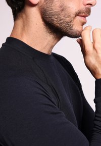 Schwarzes Langarmshirt mit Rundhalsausschnitt, aus glattem, elastischem Stoff und sichtbaren Nahtdetails an den Schultern.