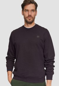 Donkerpaarse sweatshirt met ronde hals, ribbelmanchetten en -zoom. Bevat een klein, getextureerd logo op de linkerborst. Soepele stoftextuur.