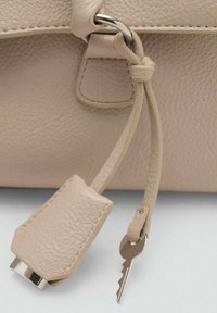 Beige leren tas detail met een gestructureerde afwerking, een zilveren bevestigingsring en een sleutel vastgezet met een bijpassende leren strap.