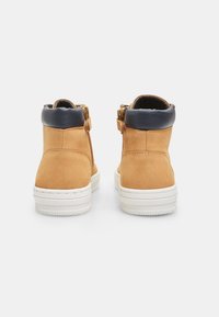 Botas de tobillo de ante en color beige con un puño de piel de color azul marino, con cremalleras laterales y suelas de goma blanca. Superficie texturizada con un acabado suave.