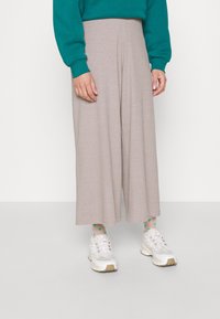Beige vida byxor i en ribbad textur, tillsammans med en teal sweatshirt och vita sneakers med beige accenter.