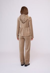 Beżowy dres z weluru, składający się z kurtki z kapturem z detalem w postaci peplum oraz dopasowanych spodni z ściągaczami. Miękka faktura, luźny krój.