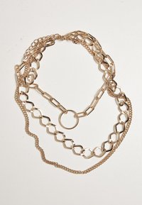 Guldtonet lagdelt kædehalssmykke med forskellige linkformer, herunder oval og hexagonal, med en glat finish og en central ringdetalje.