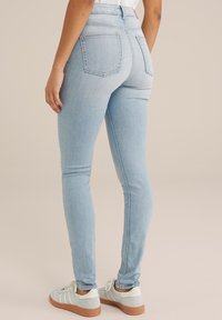 Svetlo modri visokotega ožji kavbojke z zadnjimi žepi in mehkimi denim teksturami, v kombinaciji s svetlo modrimi superge, ki imajo smetanaste poudarke.