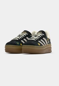 Adidași negri cu dungi albe, tălpi platformă, broderie florală galbenă și albastră și accente bej pe limbă și guler.