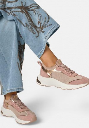 Legs wearing blue jeans with brown embroidery and rose gold and beige chunky sneakers with thick white soles.