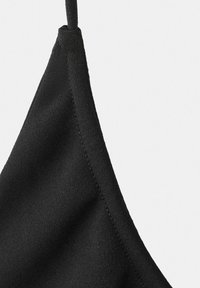 Posnetek črne tkanine oblačila z tankim trakom in vidnim šivom na enostavni svetli podlagi.